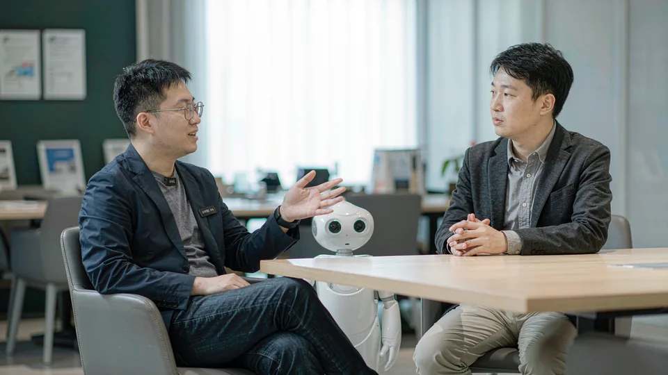 会议室里的一对一专访：来访客人正在提问，桌上摆着一台人形机器人