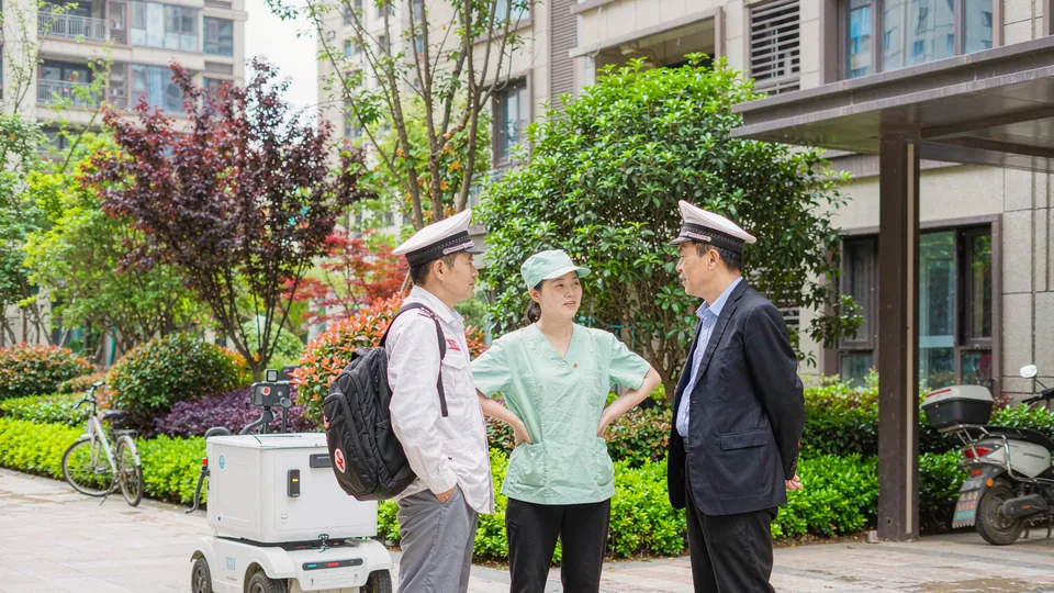 社区院子里：物业管家、护工与保洁人员站在服务机器人旁交谈